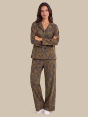 A woman modeling a two-piece pajama set with a brown paisley pattern, featuring a long-sleeve button-up top and matching pants, against a solid beige background.