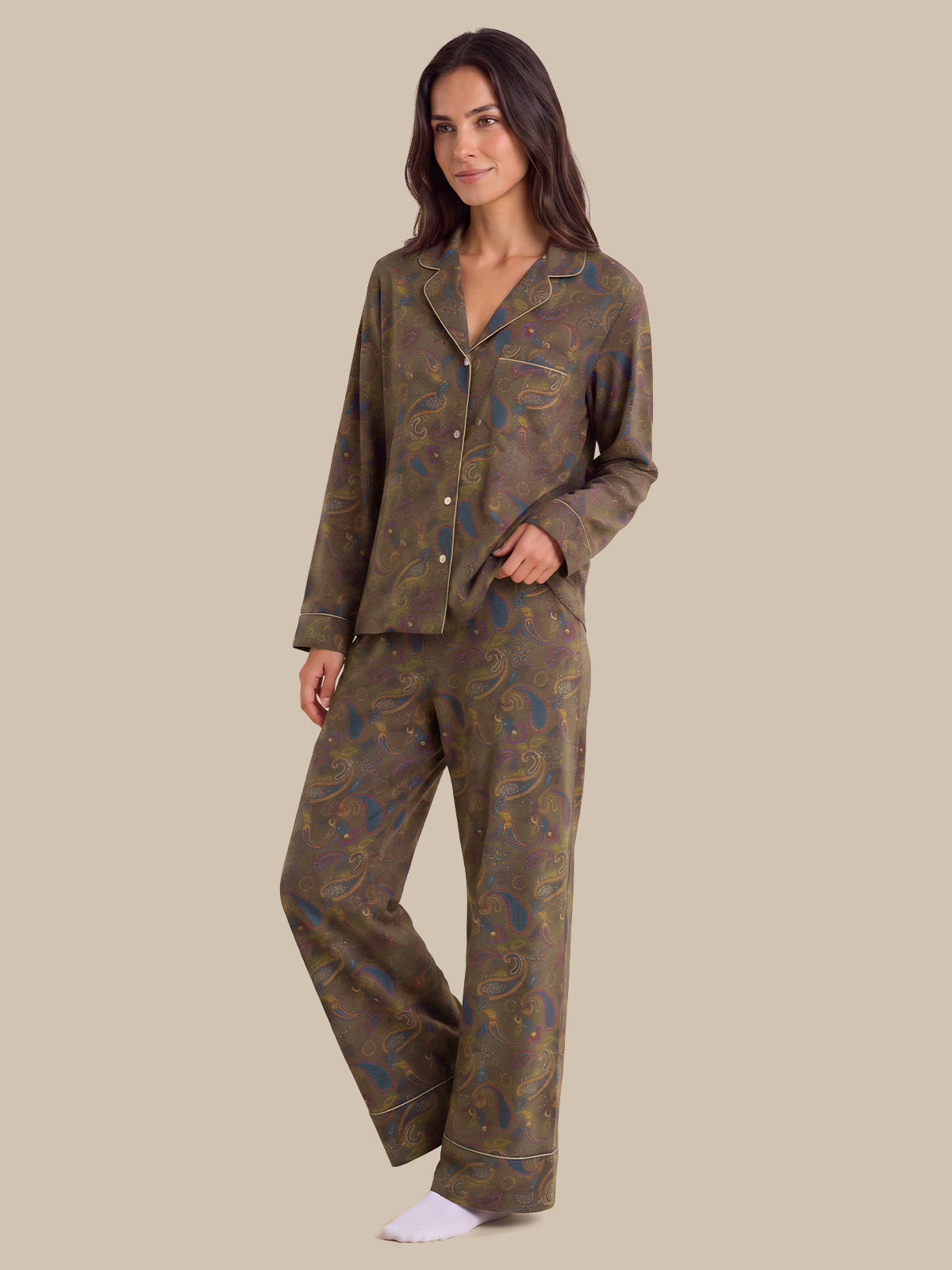 A woman modeling a two-piece pajama set with a long-sleeve button-front top and matching wide-leg pants, featuring an abstract paisley-like pattern in olive green, brown, and blue on a solid beige background.