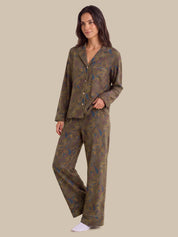 A woman modeling a two-piece pajama set with a long-sleeve button-front top and matching wide-leg pants, featuring an abstract paisley-like pattern in olive green, brown, and blue on a solid beige background.