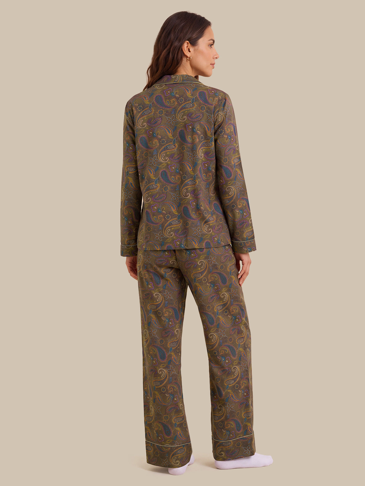 A woman shown from the back wearing a matching long-sleeve pajama set with an intricate paisley pattern in olive green, gold, and blue, paired with white socks, against a solid beige background.