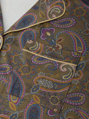 A close-up of a paisley-patterned fabric garment, likely a jacket or coat, featuring a brown base with intricate paisley motifs in purple, blue, yellow, and orange, accented by light beige piping.