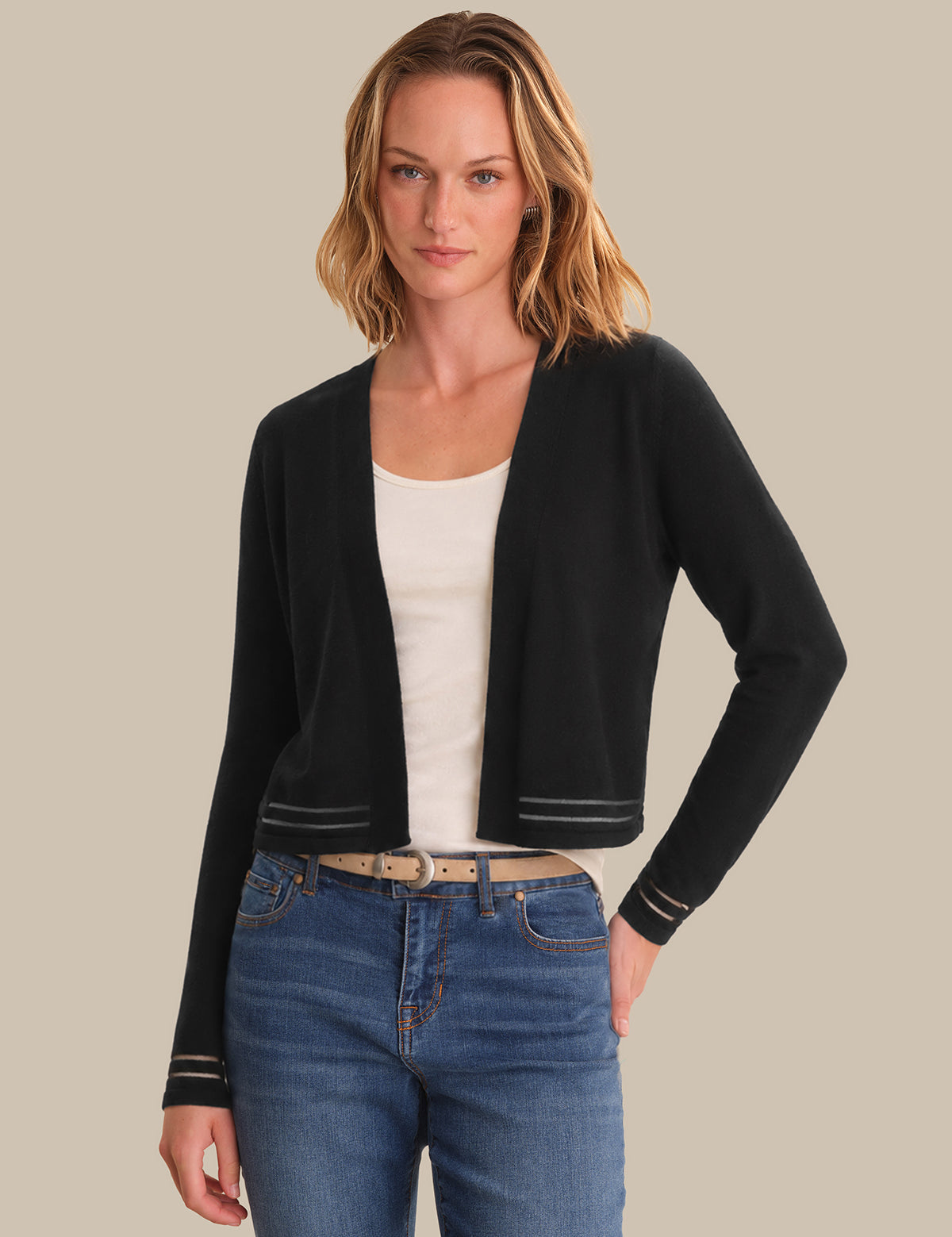 Woman wearing a black cardigan over a white top and blue jeans on a beige background