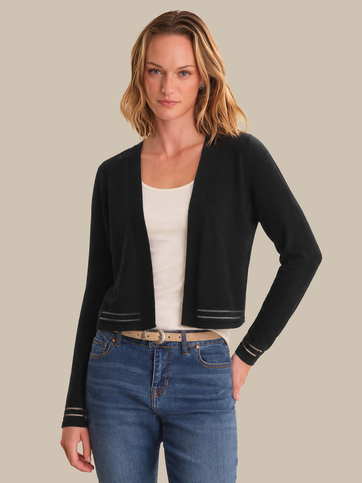 Woman wearing a black cardigan over a white top and blue jeans on a beige background