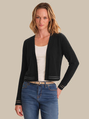Woman wearing a black cardigan over a white top and blue jeans on a beige background