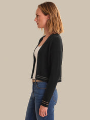 Woman wearing a black cardigan over a white shirt and blue jeans on a beige background