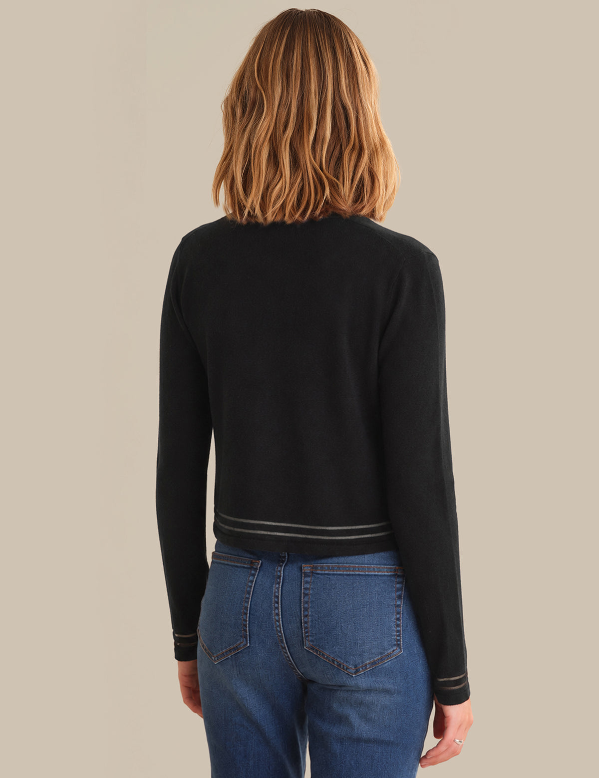 Person wearing a black long-sleeve top and blue jeans on a beige background