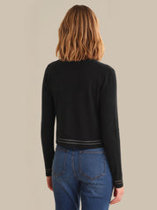 Person wearing a black long-sleeve top and blue jeans on a beige background