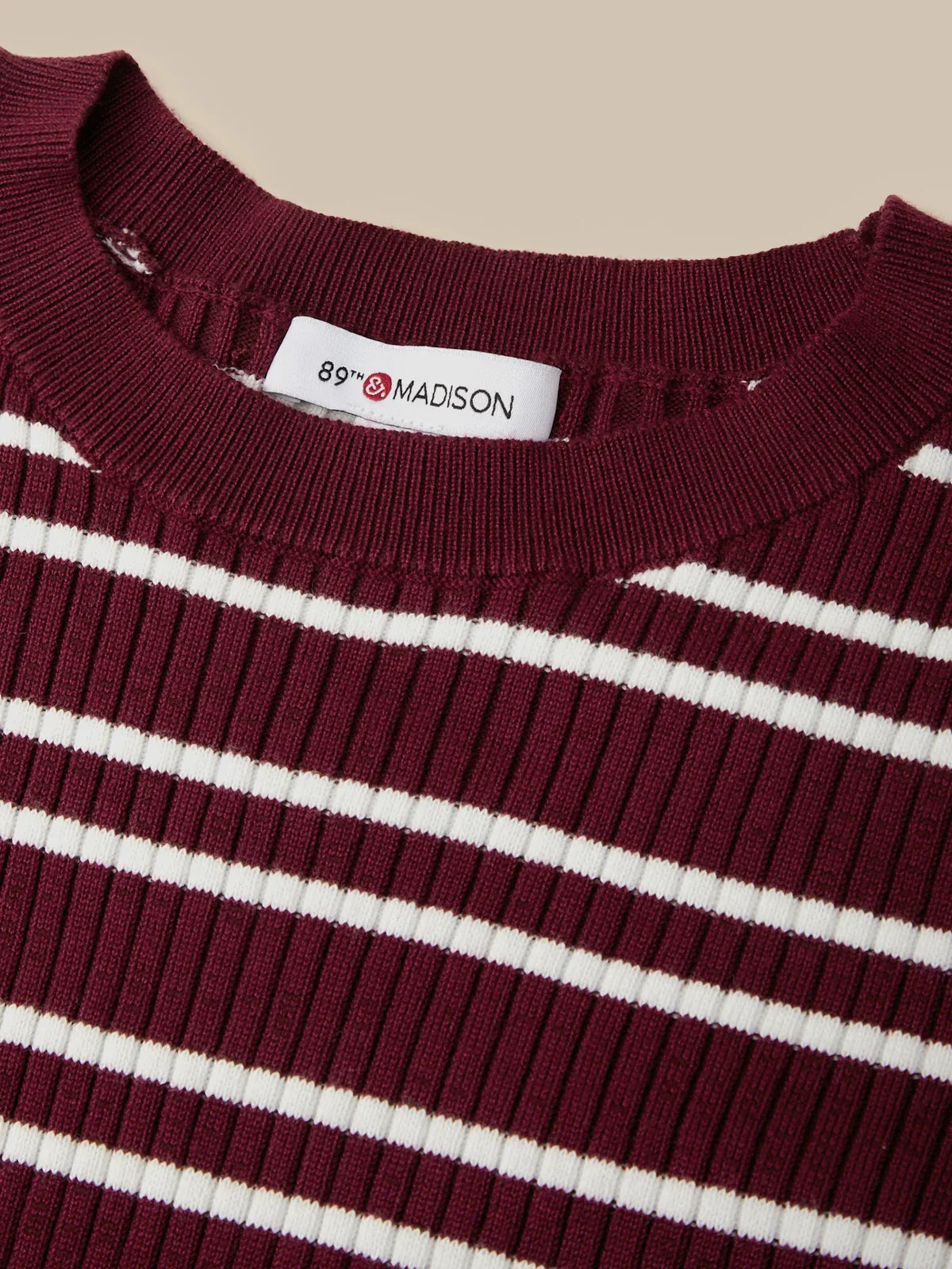 Close-up of a ribbed knit crewneck sweater with horizontal burgundy and white stripes, featuring a white neck label that reads '89th & MADISON'.