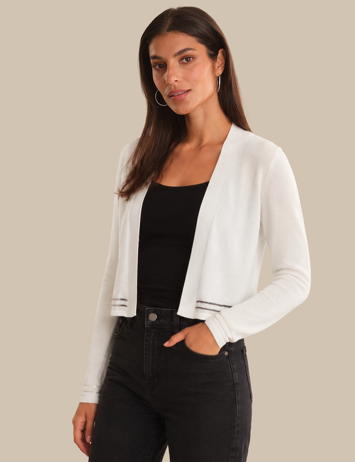 Woman wearing a white cardigan over a black top and jeans on a beige background