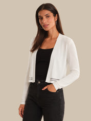 Woman wearing a white cardigan over a black top and jeans on a beige background