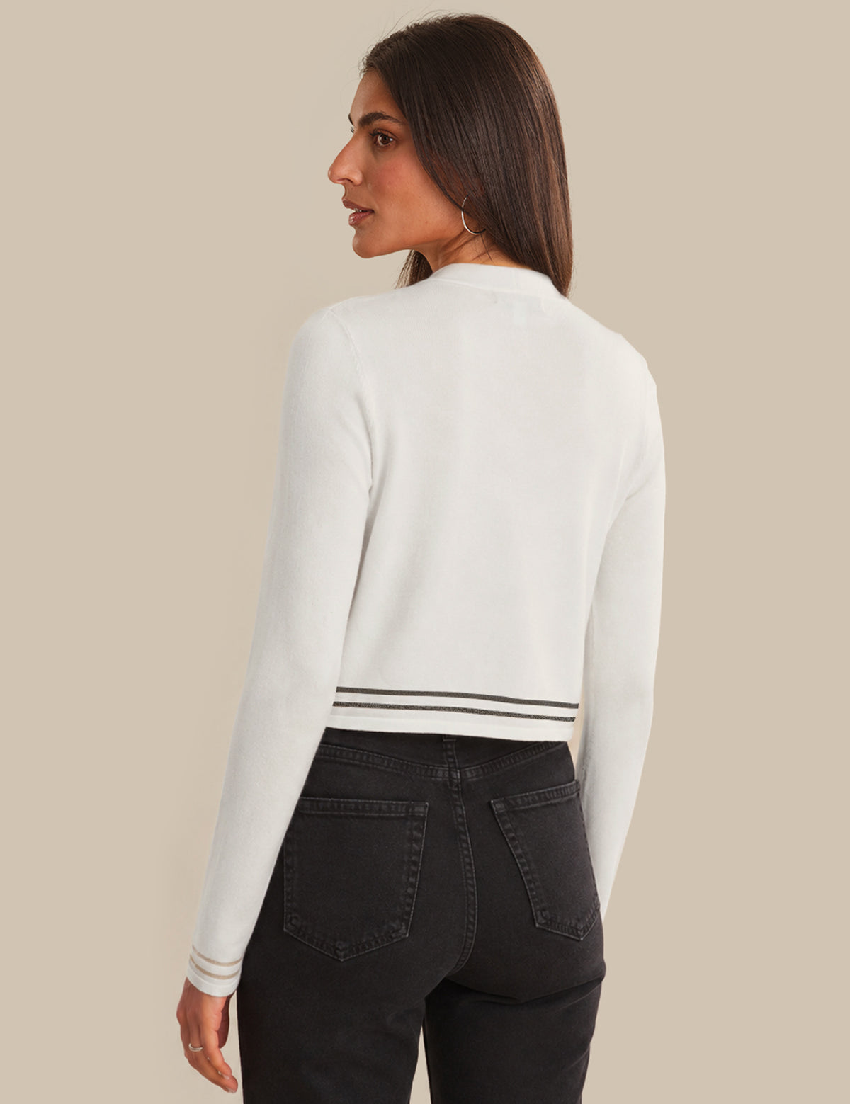 Woman wearing a white sweater and black pants against a beige background