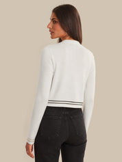 Woman wearing a white sweater and black pants against a beige background