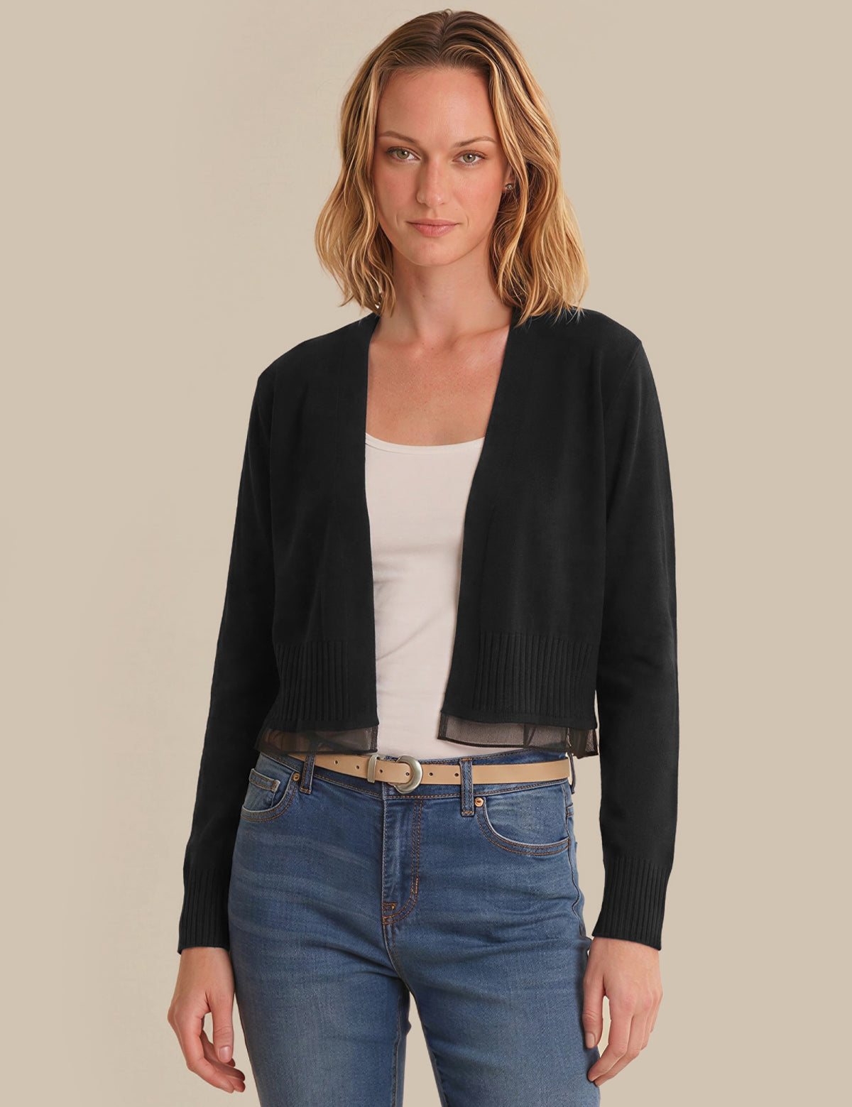 Woman wearing a black cardigan over a white top and blue jeans on a beige background