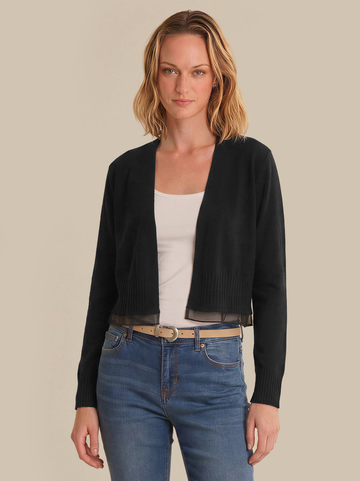Woman wearing a black cardigan over a white top and blue jeans on a beige background
