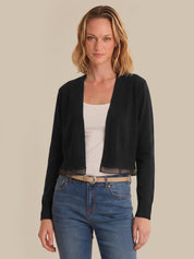 Woman wearing a black cardigan over a white top and blue jeans on a beige background