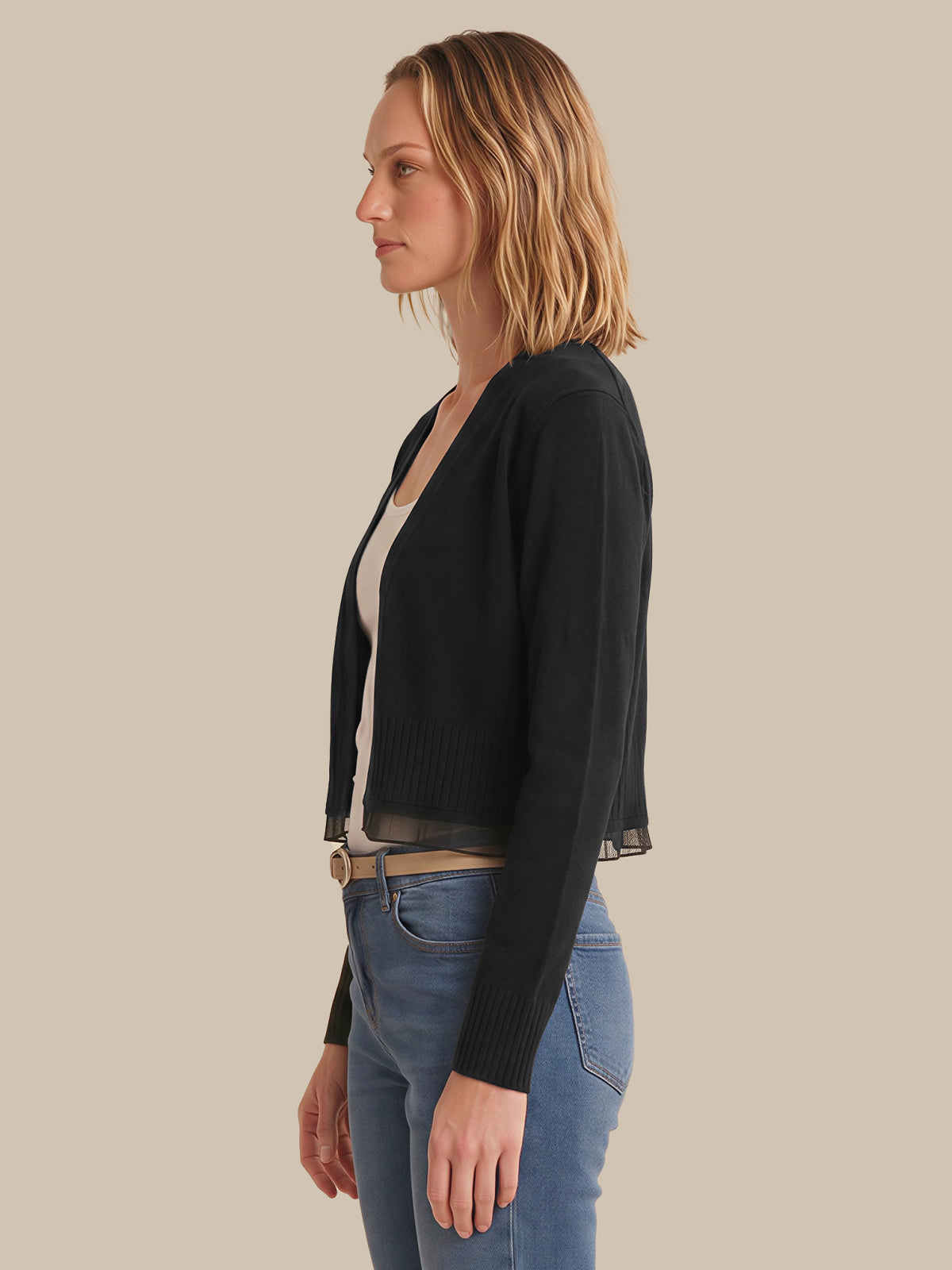 Woman wearing a black cardigan over a white top and blue jeans on a beige background