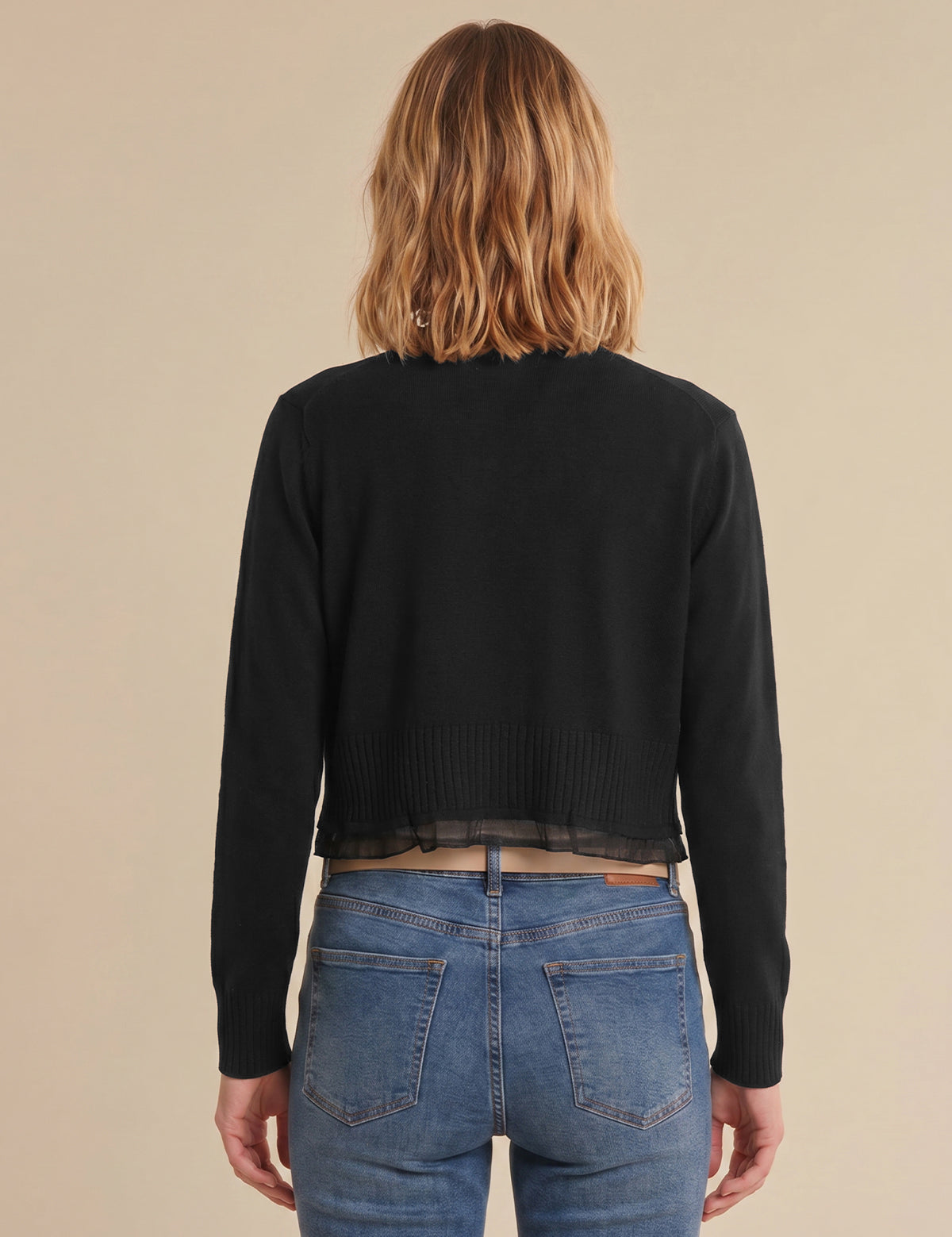 Person wearing a black cardigan and blue jeans from behind on a beige background