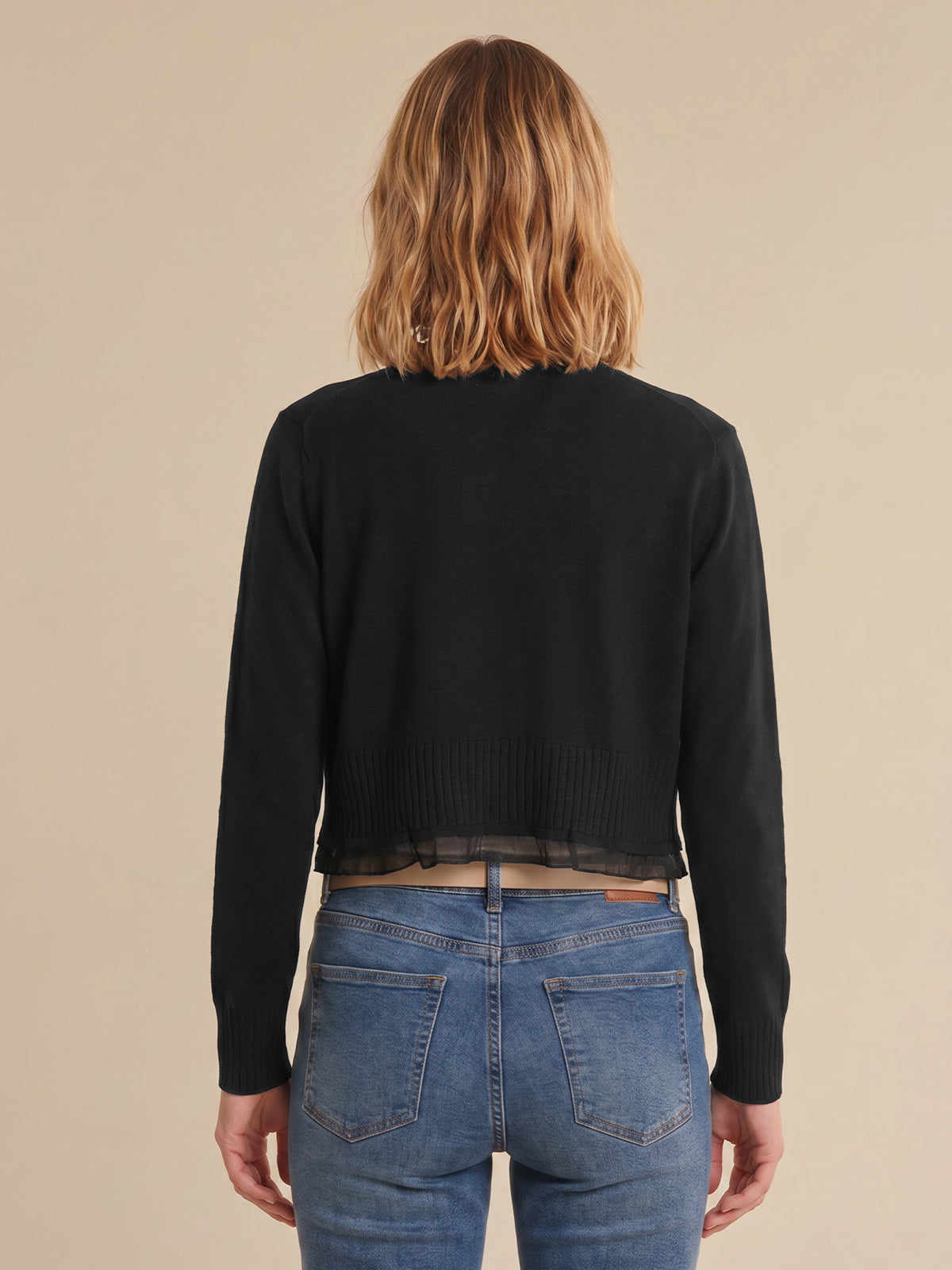 Person wearing a black cardigan and blue jeans from behind on a beige background