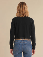 Person wearing a black cardigan and blue jeans from behind on a beige background