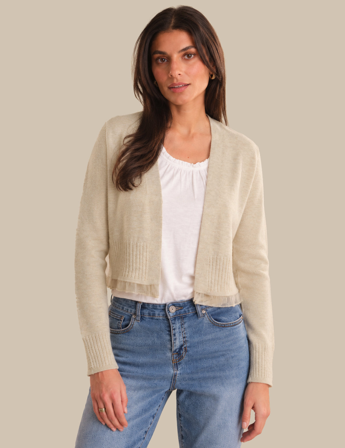 Woman wearing a beige cardigan over a white top and blue jeans on a beige background