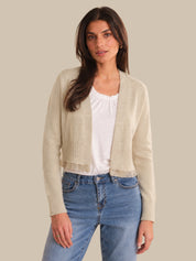 Woman wearing a beige cardigan over a white top and blue jeans on a beige background