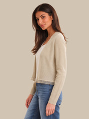 Woman wearing a beige cardigan over a white shirt with blue jeans on a beige background