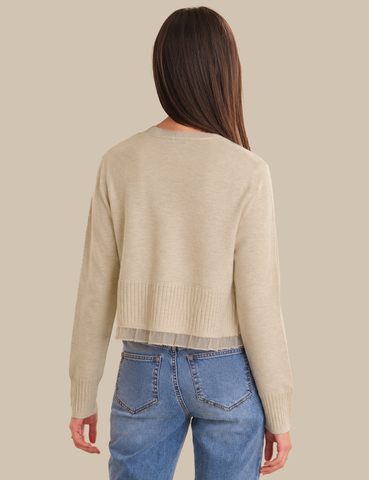 Person wearing a beige cardigan and blue jeans on a beige background