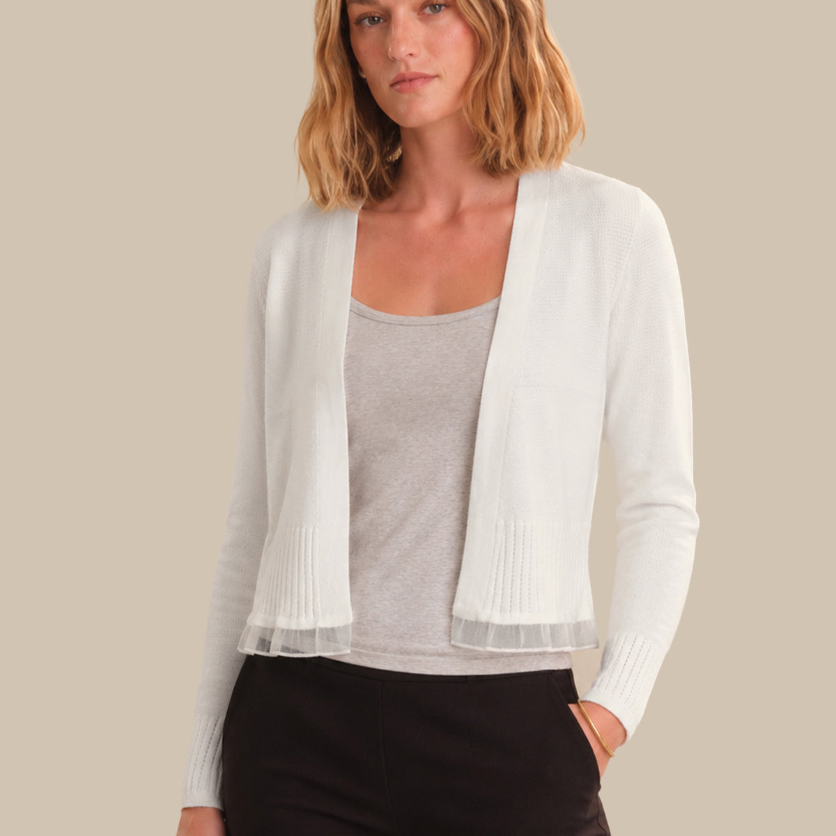 Woman wearing a white cardigan over a gray top and black pants on a beige background