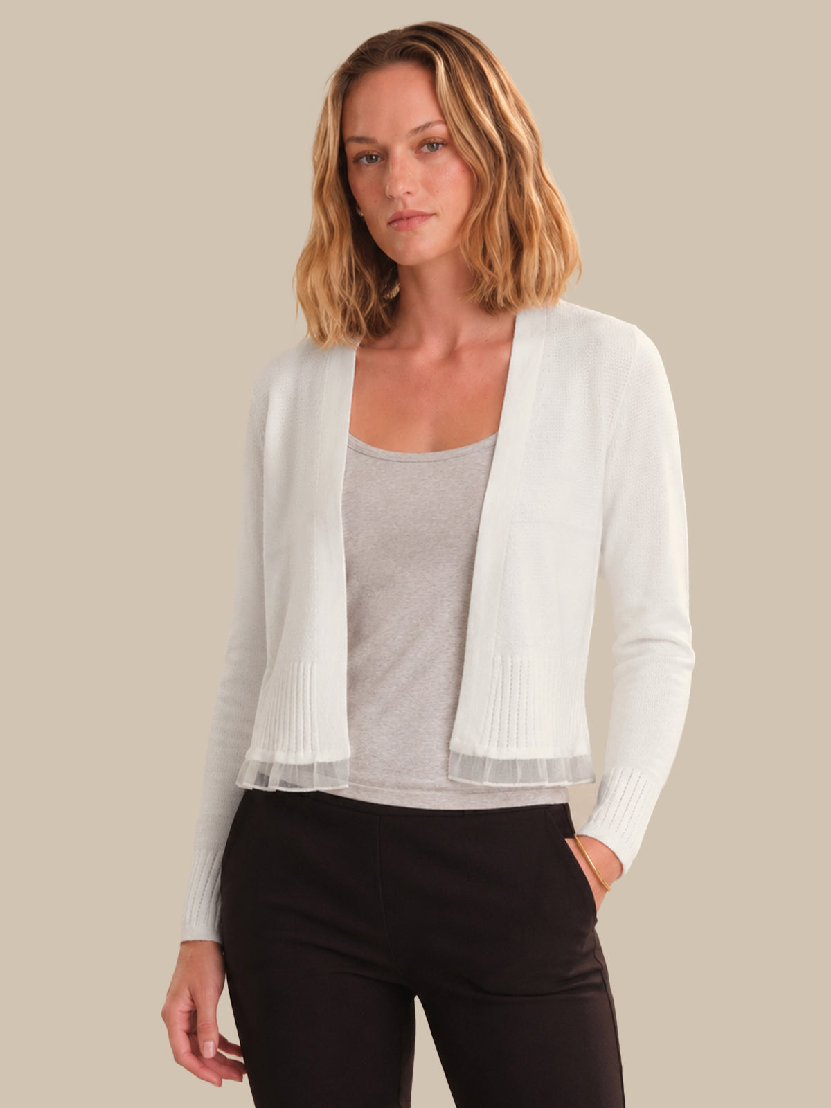 Woman wearing a white cardigan over a gray top and black pants on a beige background