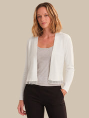 Woman wearing a white cardigan over a gray top and black pants on a beige background