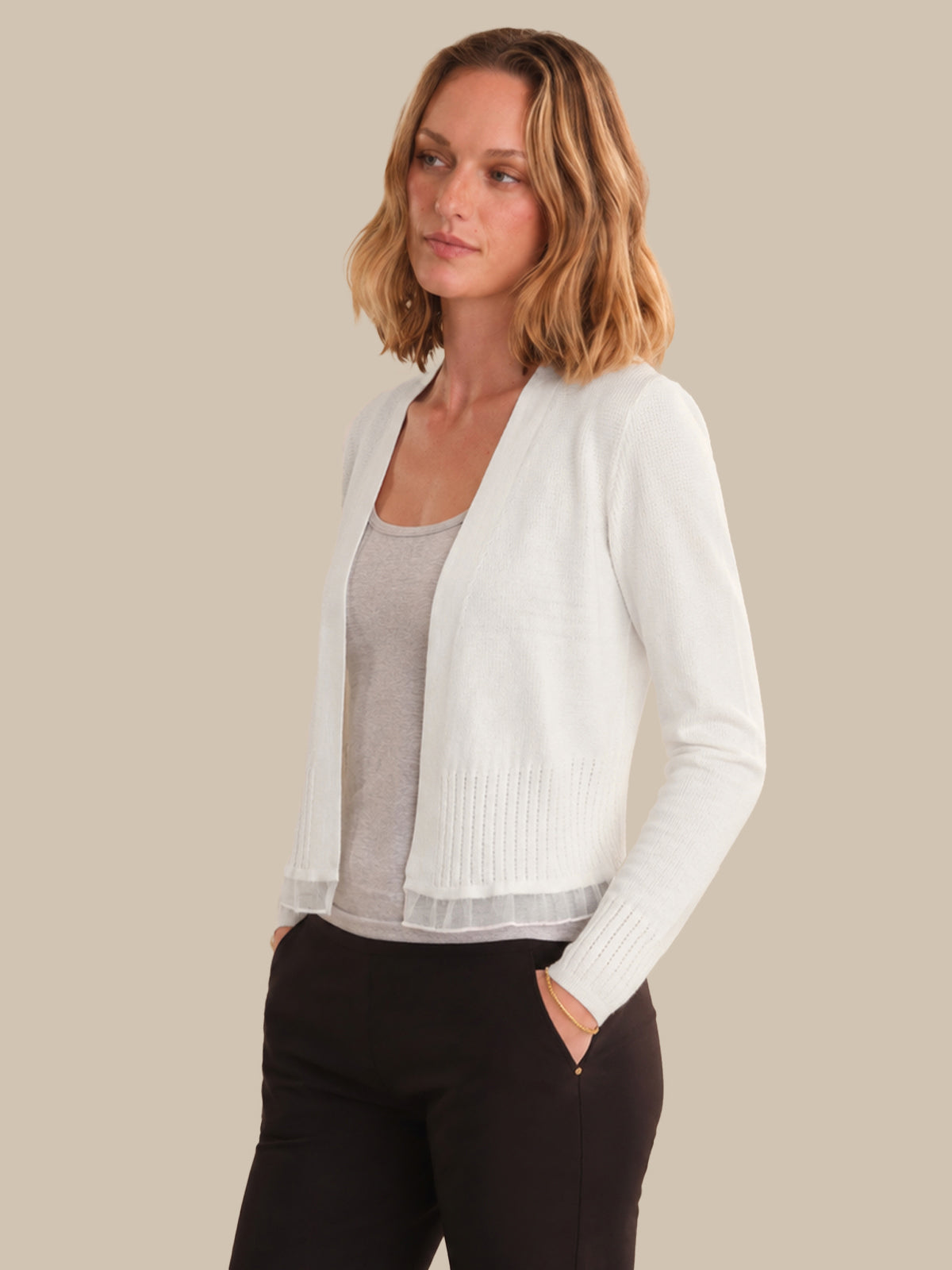Woman wearing a white cardigan over a gray top and black pants on a beige background