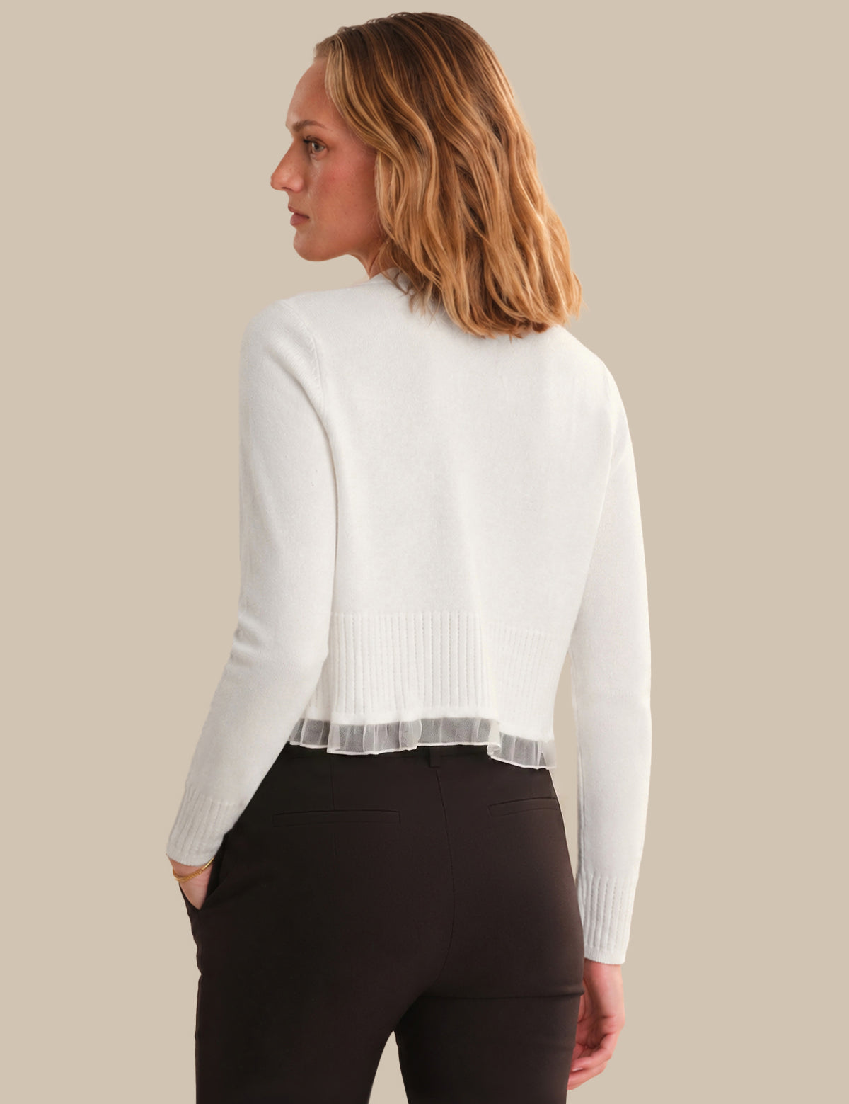 Woman wearing a white sweater with sheer panels on a beige background