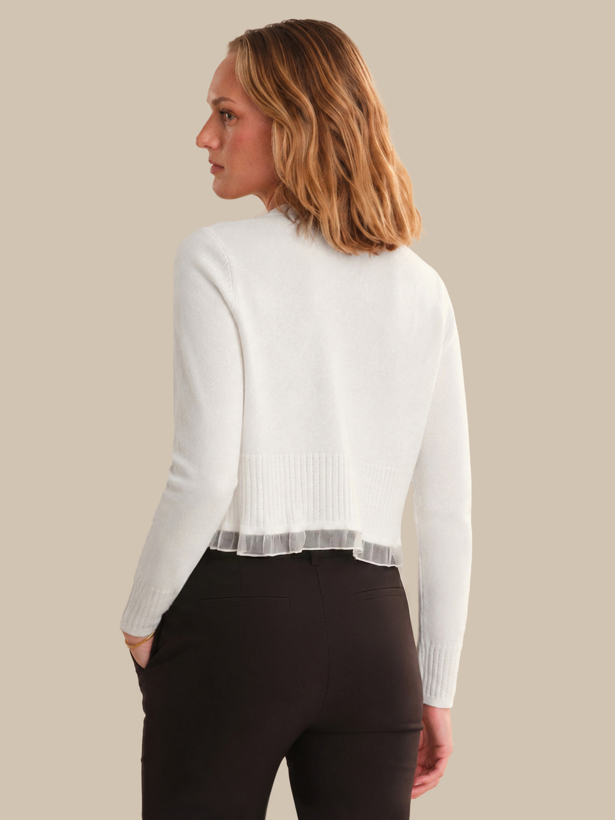 Woman wearing a white sweater with sheer panels on a beige background