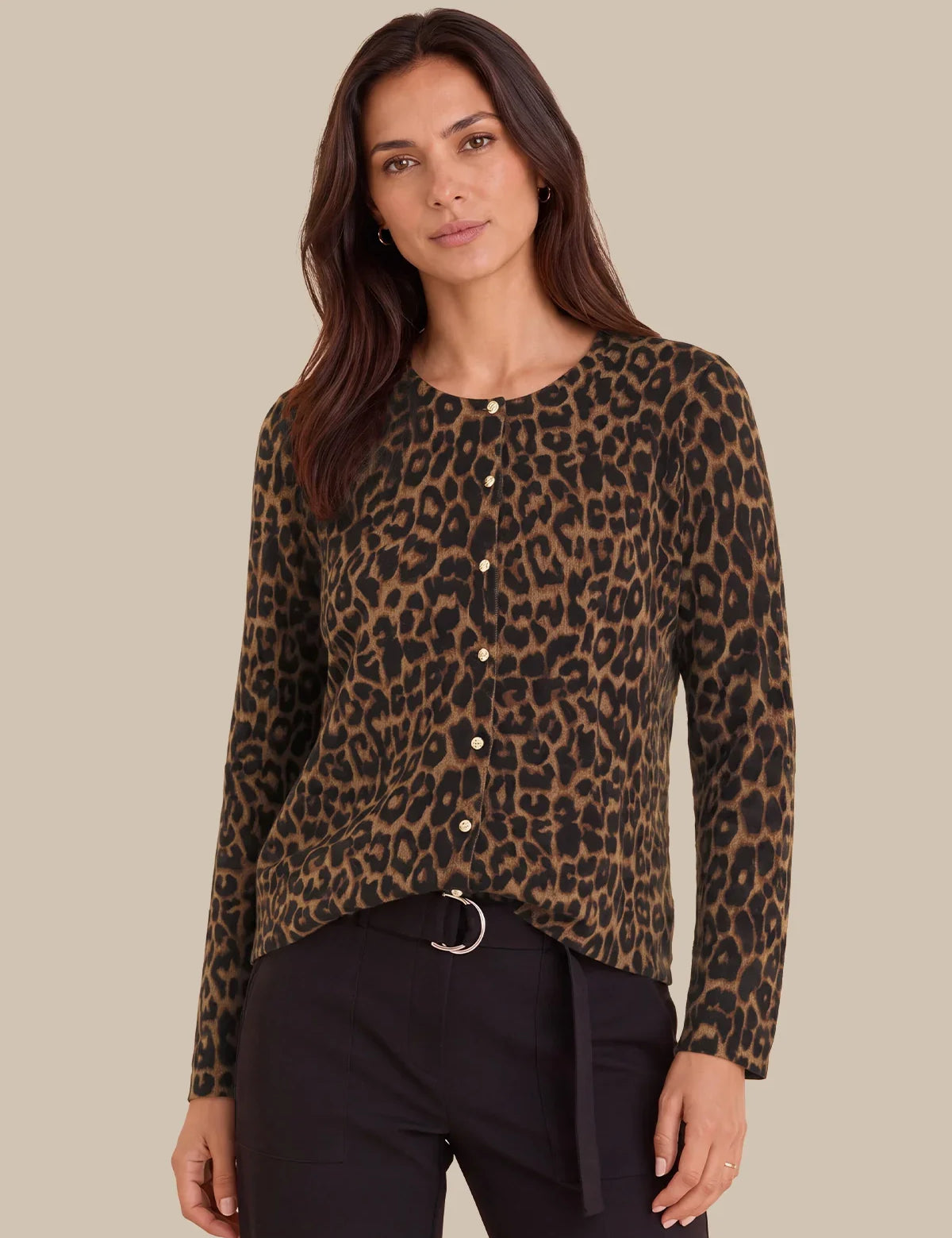 A woman modeling a long-sleeve leopard print knit top with a button-up front, paired with black pants, against a solid beige background.