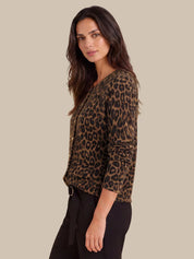 A woman modeling a leopard-print cardigan with three-quarter sleeves, paired with black pants, against a solid beige background.