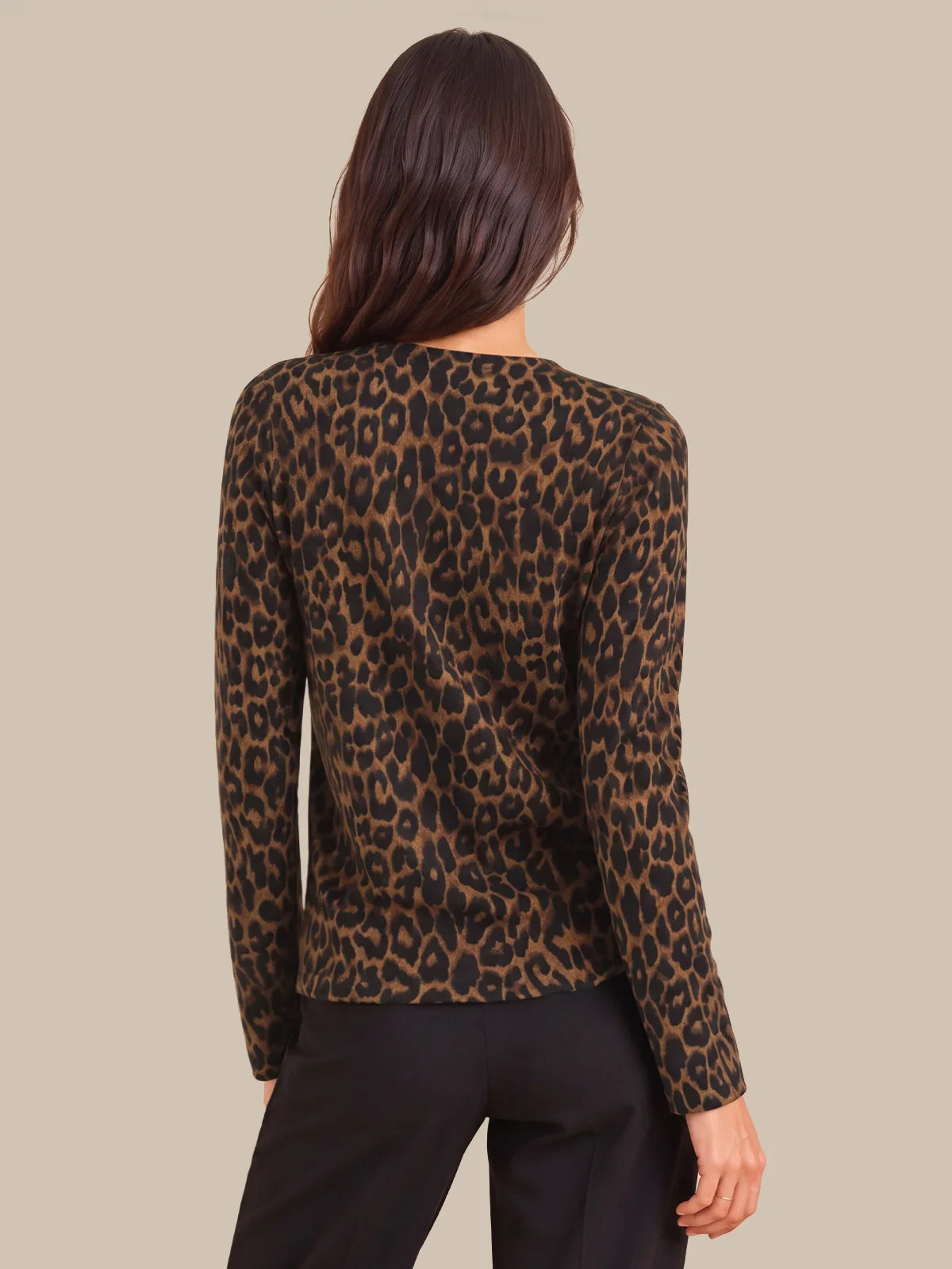 A woman shown from the back wearing a leopard-print long-sleeve top and black pants against a solid beige background.