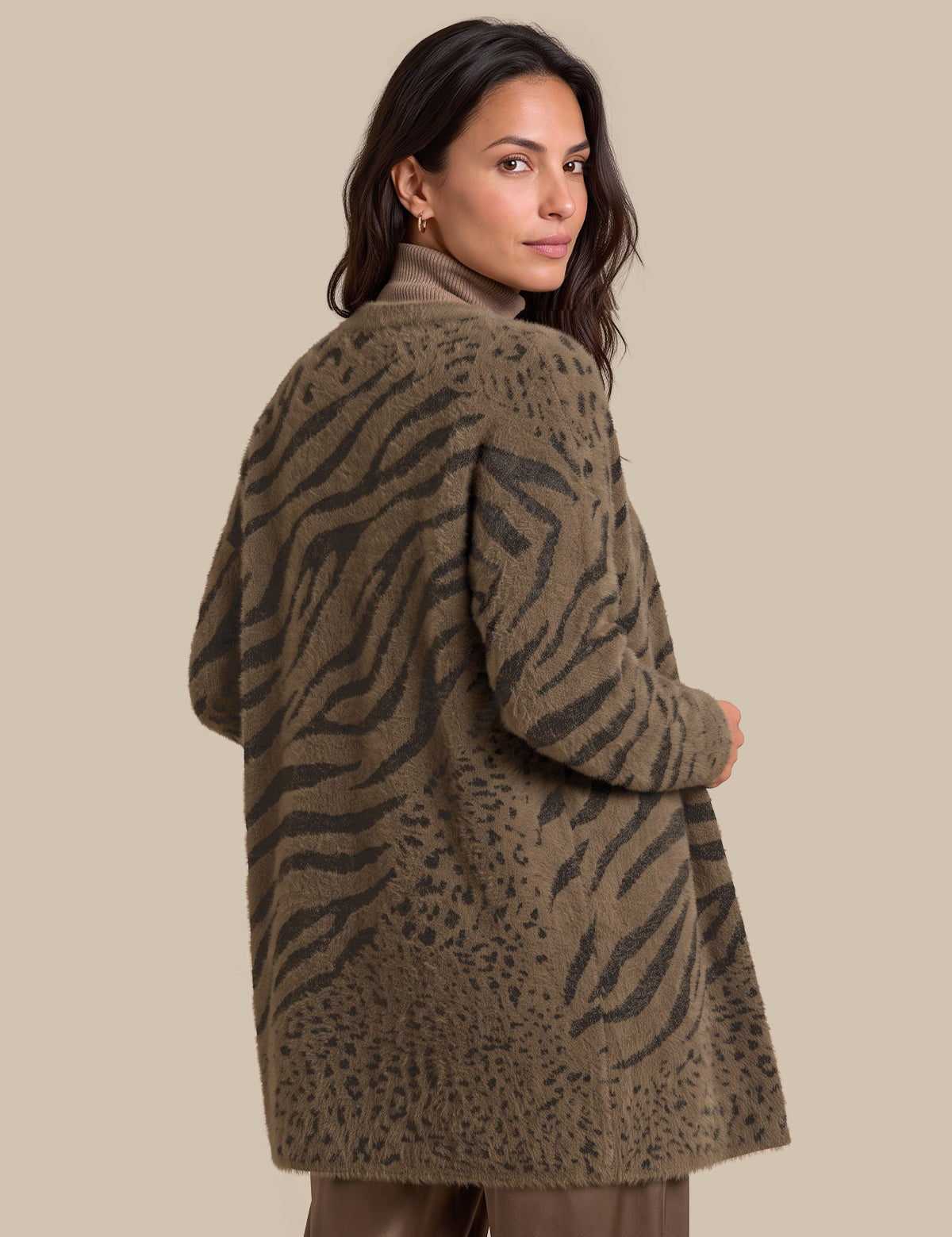 A woman wearing a fuzzy, open-front cardigan with a brown and olive green animal print pattern, photographed against a solid beige studio background.