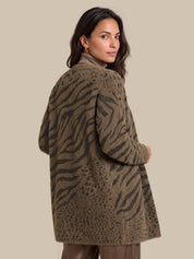 A woman wearing a fuzzy, open-front cardigan with a brown and olive green animal print pattern, photographed against a solid beige studio background.