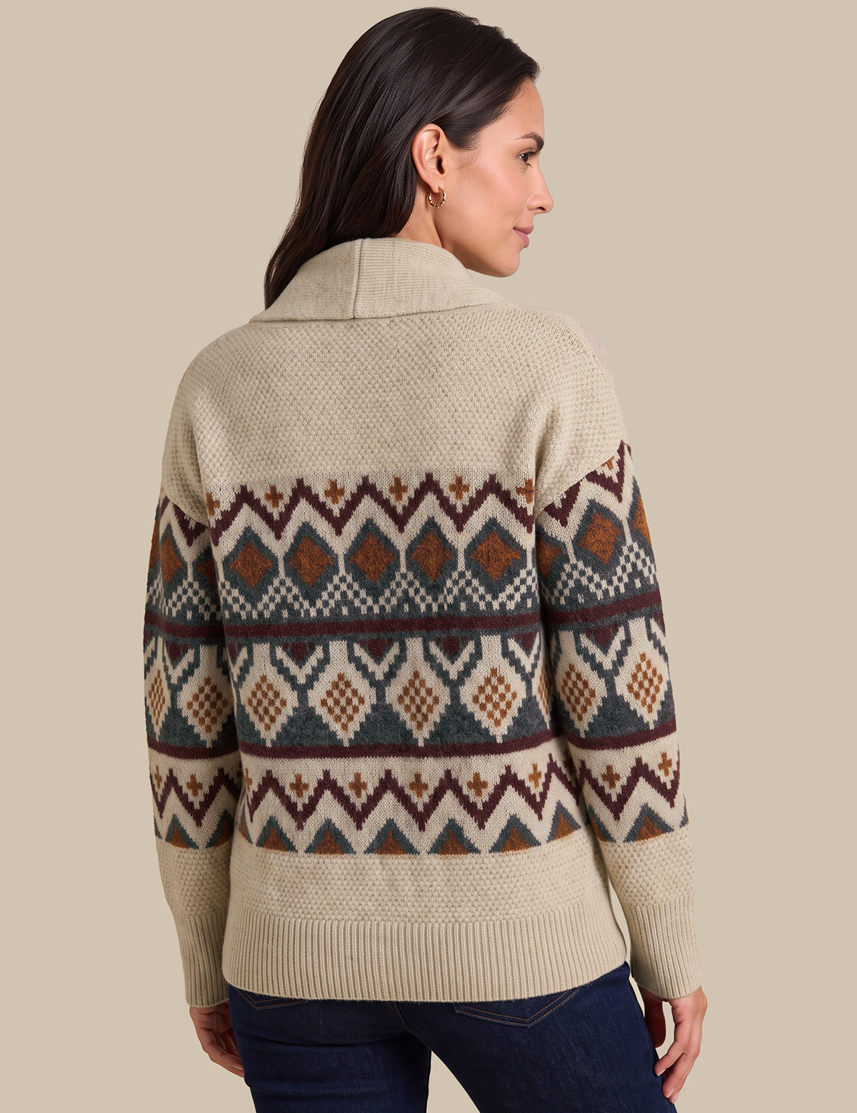 A woman shown from the back wearing a cream-colored knit sweater with a colorful geometric Fair Isle pattern across the shoulders, upper back, and sleeves, paired with dark blue jeans against a solid beige background.