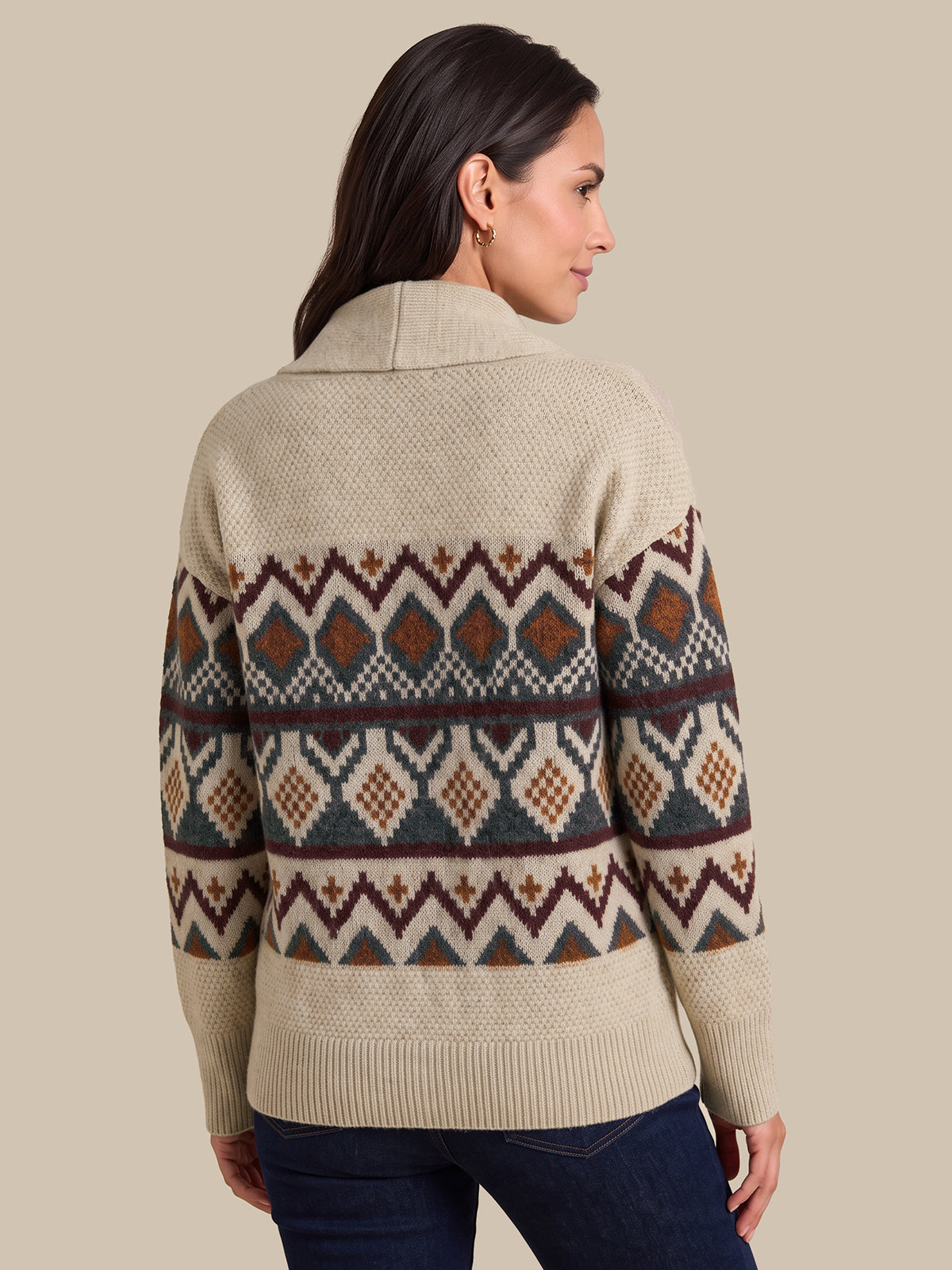 A woman shown from the back wearing a cream-colored knit sweater with a colorful geometric Fair Isle pattern across the shoulders, upper back, and sleeves, paired with dark blue jeans against a solid beige background.