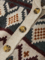 Close-up of a knit cardigan with a geometric Fair Isle pattern in cream, slate blue, burgundy, and rust orange, featuring translucent amber buttons.