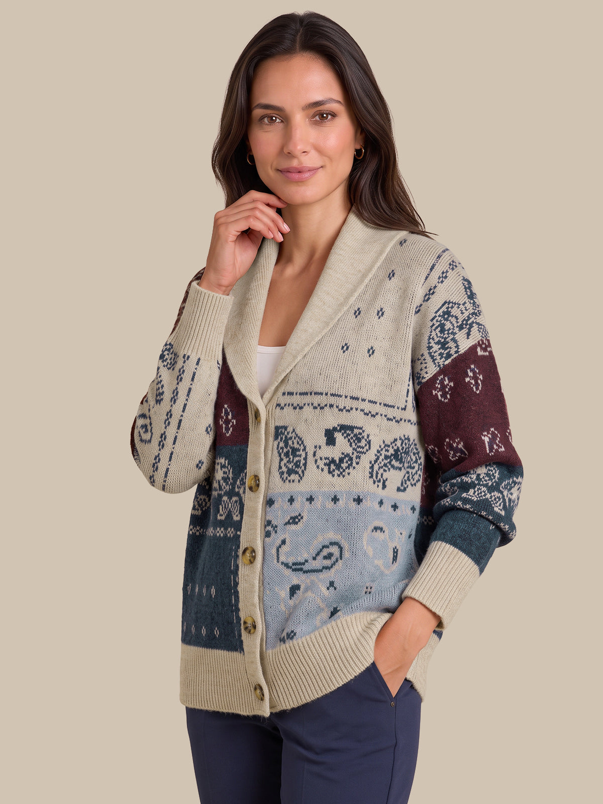 A woman modeling a multi-colored knit cardigan sweater with a shawl collar, button front, and intricate paisley patterns in beige, blue, and burgundy, set against a solid beige background.