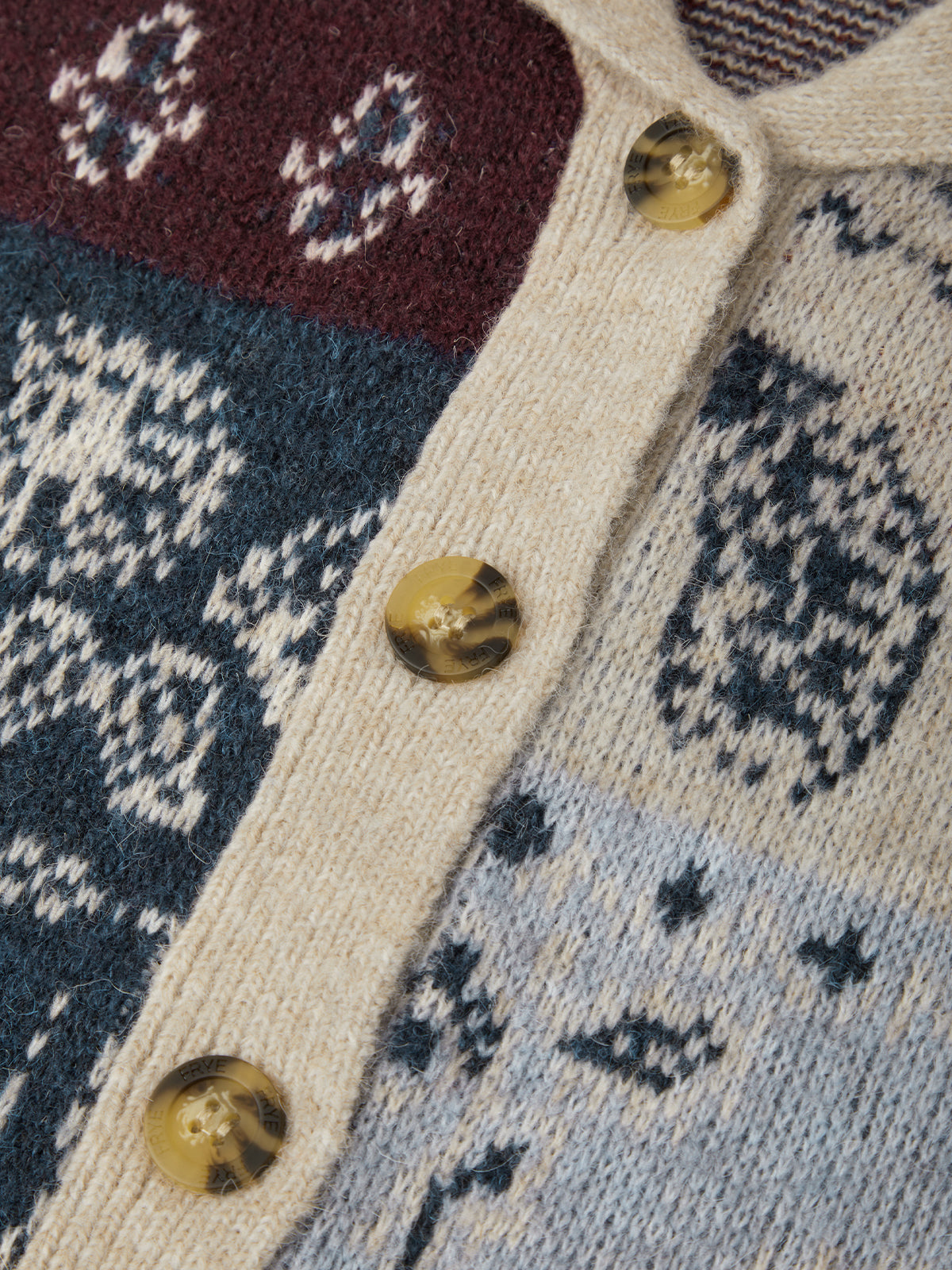 Close-up of a knitted cardigan with patchwork Fair Isle patterns in cream, navy, burgundy, and light blue, featuring amber-colored buttons.
