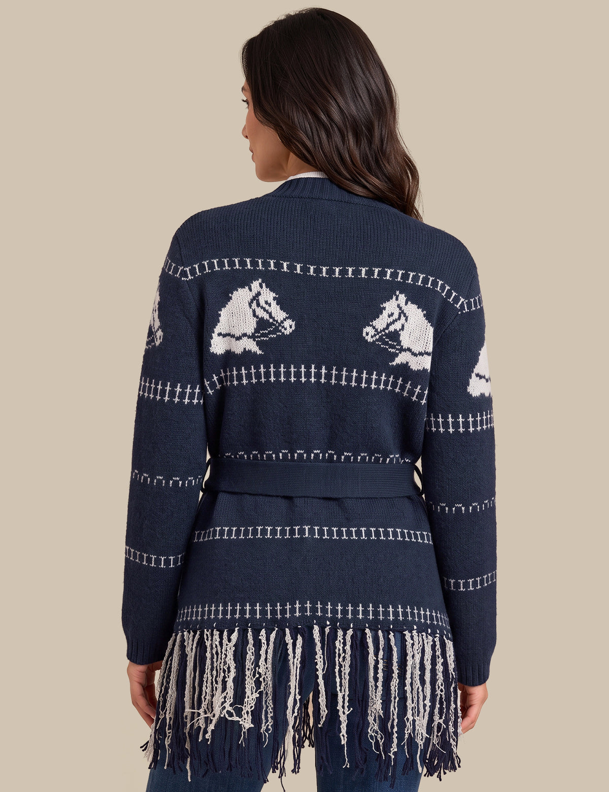 A woman shown from the back wearing a navy blue knit cardigan with white horse motifs and fringe trim, against a solid beige background.