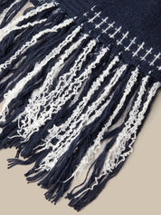 Close-up of a woven textile with dark navy blue and off-white stripes and long fringe tassels, shown against a plain beige background.