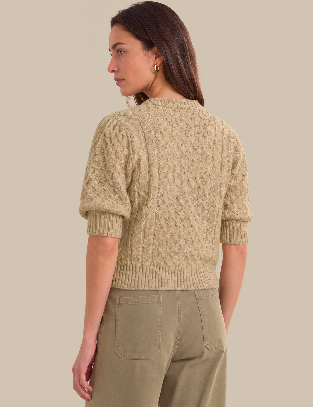 A woman shown from the back wearing a textured short-sleeve knit sweater in a light beige color, paired with olive green pants, against a solid beige background.