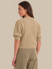 A woman shown from the back wearing a textured short-sleeve knit sweater in a light beige color, paired with olive green pants, against a solid beige background.