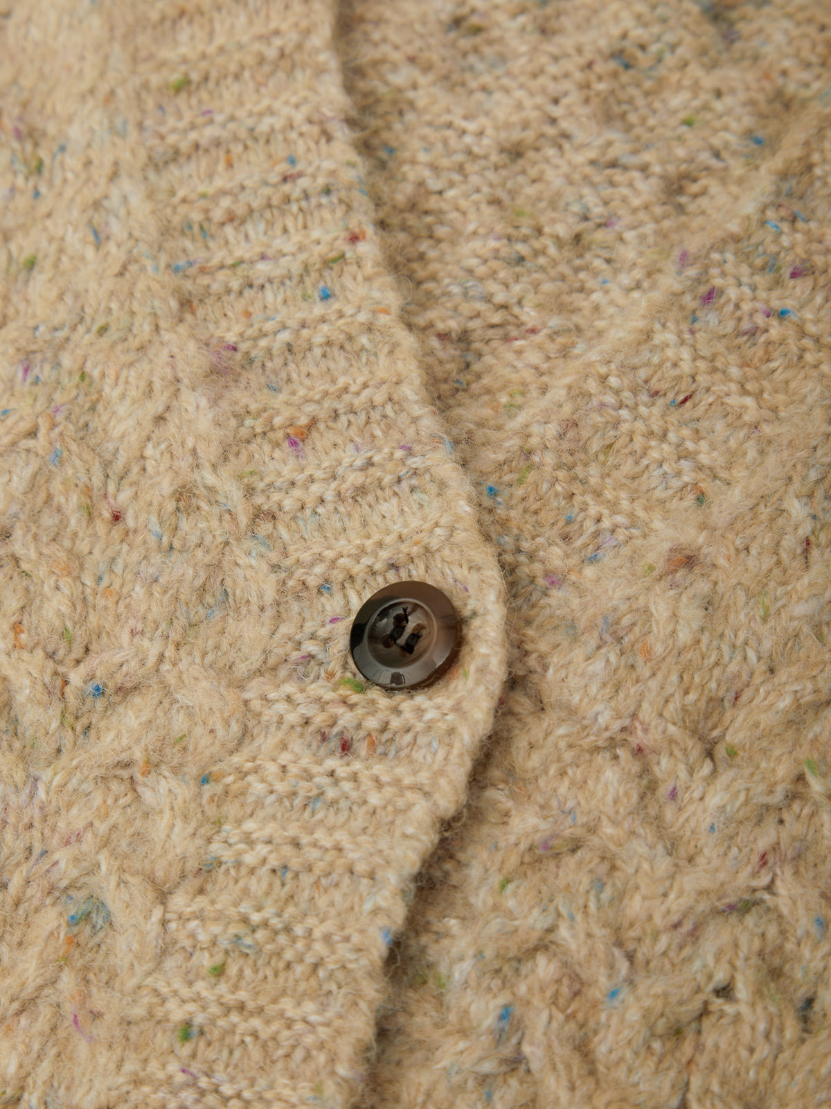 Close-up of a beige cable-knit cardigan with multicolored flecks and a dark brown button.