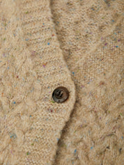 Close-up of a beige cable-knit cardigan with multicolored flecks and a dark brown button.