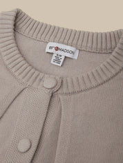Close-up of a beige knit cardigan sweater showing the ribbed collar, a white interior neck label that reads 89 MADSON, and two matching fabric buttons.